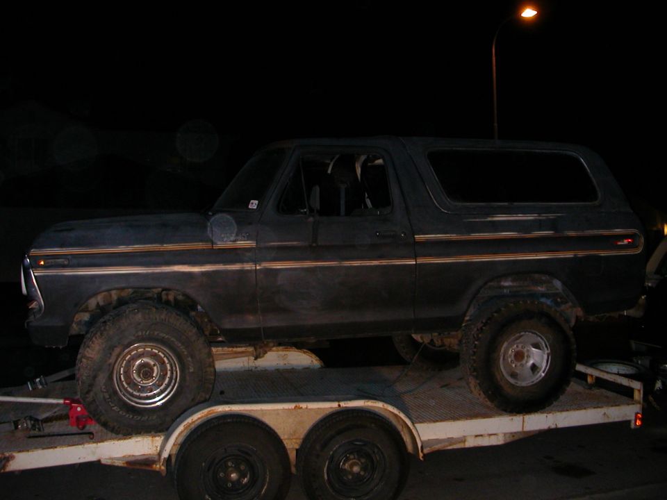 Dark blue 1978 Ford Bronco on a trailer, side view, with gold trim and off-road tires