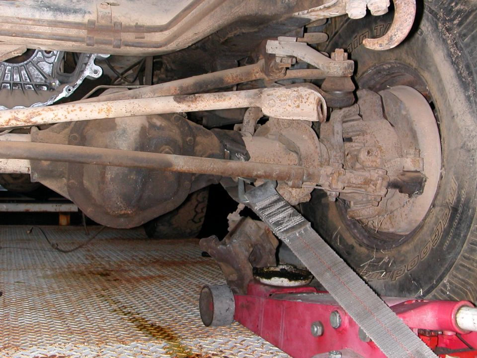 Undercarriage view of vehicle suspension and differential, with a red jack supporting it