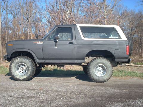 1986 Ford Bronco - This lifted Ford Bronco sits on a gravel road with trees in the background.