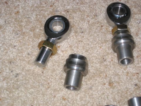 1991 Ford Explorer - Two new heim joints (rod ends) with gold-plated jam nuts laid out on carpet alongside machined steel weld-in tube bungs, one heim already t…