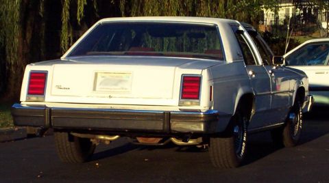 1985 Ford Crown Victoria LTD - A white sedan is parked outdoors, with another vehicle partially visible to its right.
