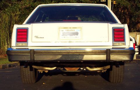 1985 Ford Crown Victoria LTD - The rear of a white 1985 Ford Crown Victoria LTD is visible, its taillights and license plate.