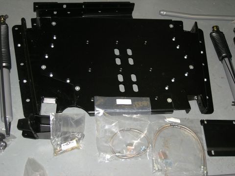 2001 Jeep Wrangler - This image displays a black skid plate, shock absorbers, and various hardware components laid out on a gray surface.