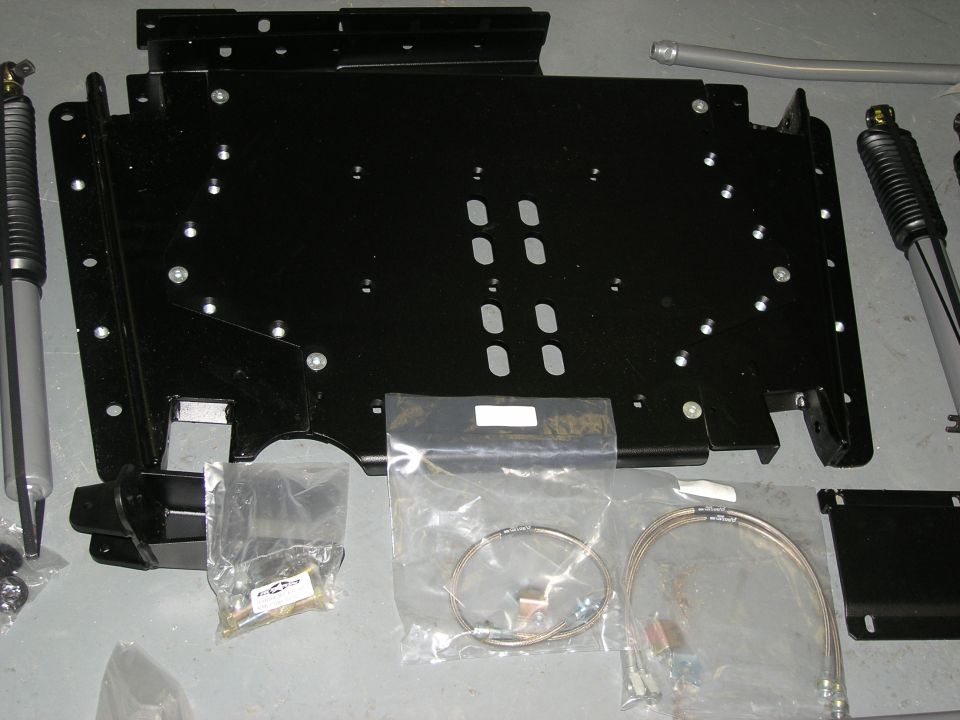 Black skid plate and two shock absorbers with hardware on a gray floor