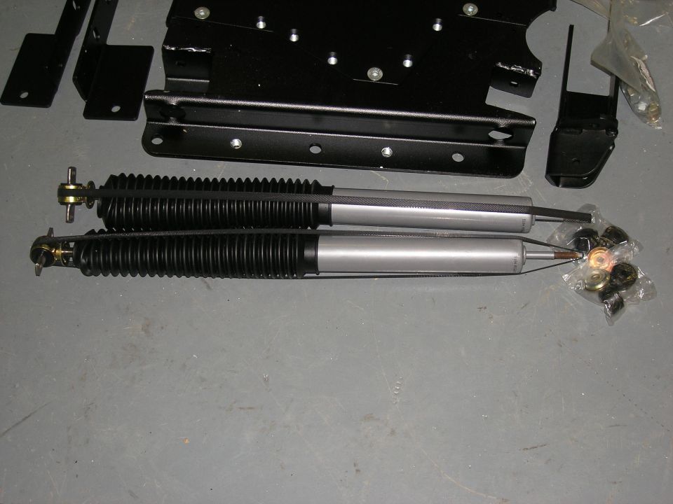 Two silver shock absorbers with black bellows and assorted metal mounting hardware in plastic bags