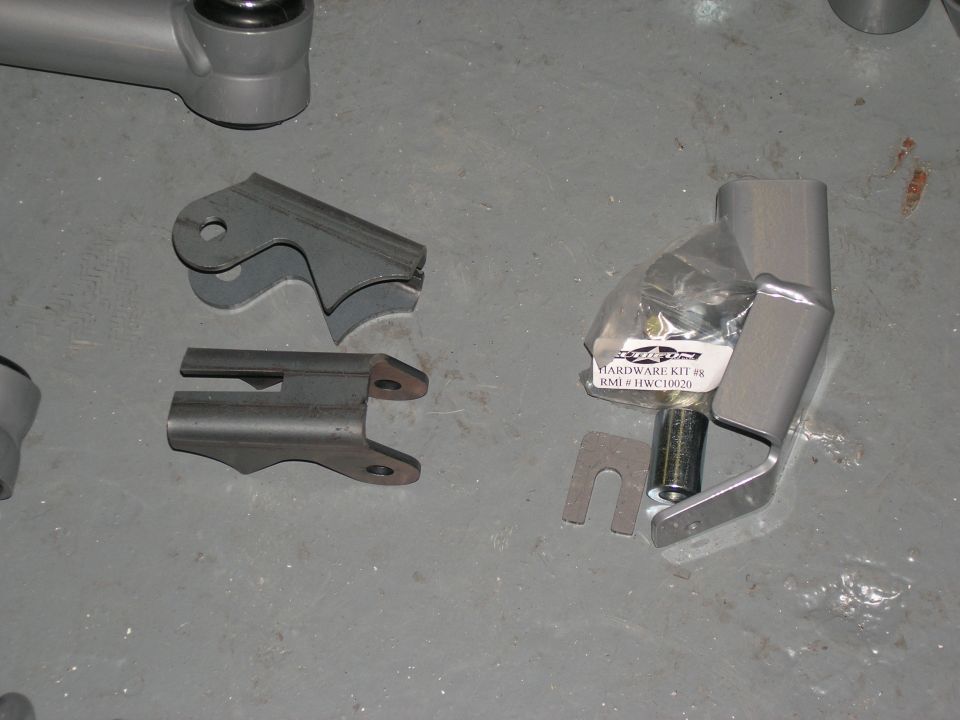 Metal brackets and a hardware kit for vehicle suspension, laid out on a gray floor