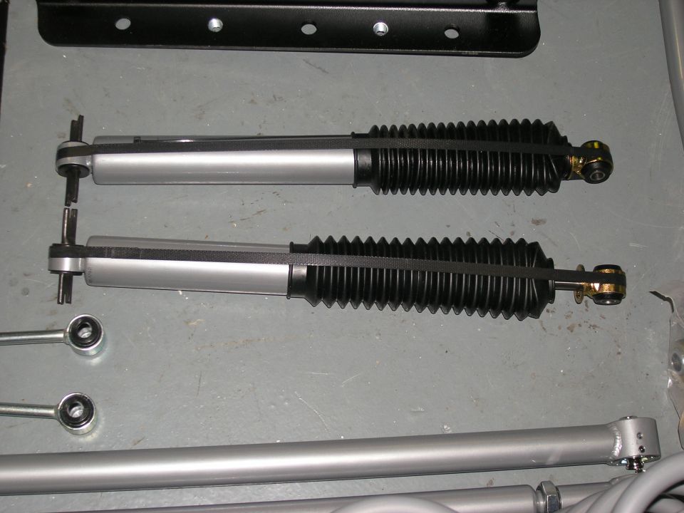 Pair of silver shock absorbers with black bellows and silver mounting hardware, on a gray surface