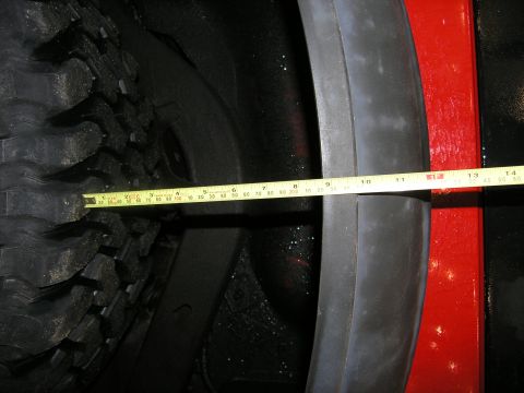 2001 Jeep Wrangler - A tape measure is used to determine the clearance between the tire and the fender of a red vehicle.