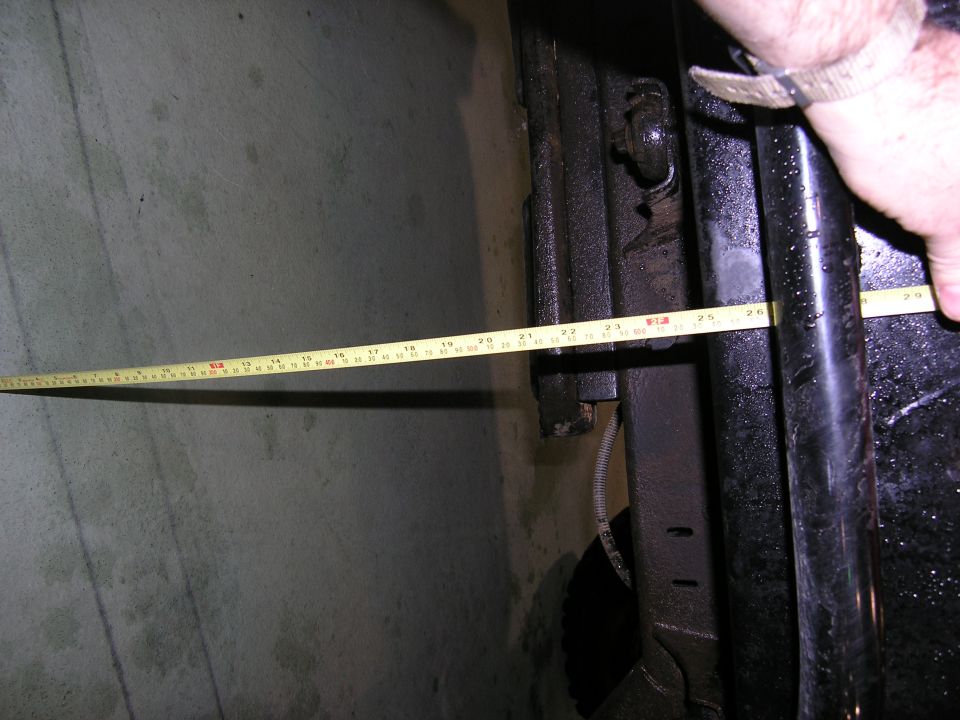 hand holding tape measure against vehicle frame, measuring length