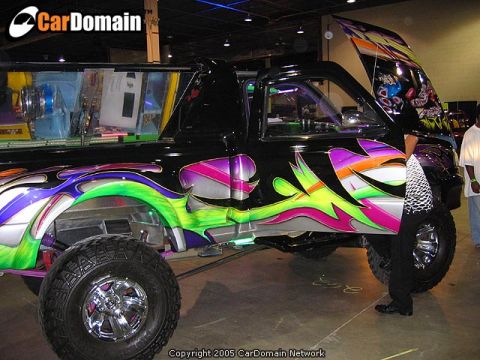 1986 Ford Bronco - This heavily customized pickup truck features vibrant flame-like graphics and an open hood displaying custom artwork.