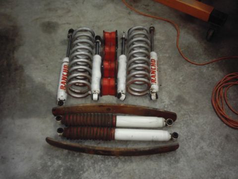 1978 Ford Bronco - A collection of Rancho shocks and coil springs, along with red polyurethane bushings and leaf springs, laid out on a concrete floor.