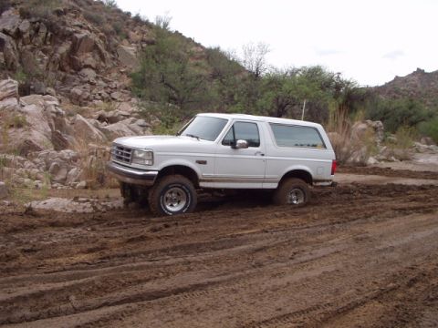 1993 Ford Bronco - A white 1992 Ford Bronco is stuck in a muddy terrain with its front wheels turned.