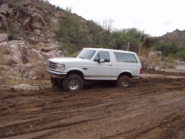 White 1990s Ford Bronco parked in churned mud on a rocky desert trail