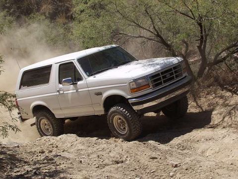 1993 Ford Bronco - White 1993 Ford Bronco navigates a dusty off-road path with trees in the background.