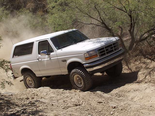 White full-size Ford Bronco climbing a dusty desert trail with mild lift and off-road tires