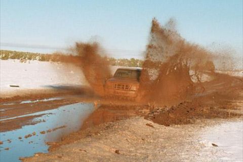 1993 Ford Bronco - A vehicle navigates a muddy obstacle, sending spray high into the air.