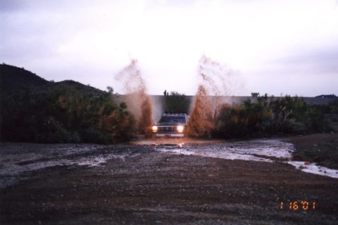 1993 Ford Bronco - A Ford Bronco navigates a water crossing, sending water and mud flying.