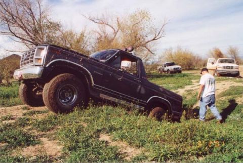 1993 Ford Bronco - Black Ford Bronco stuck in a ditch with two other trucks visible in the background.
