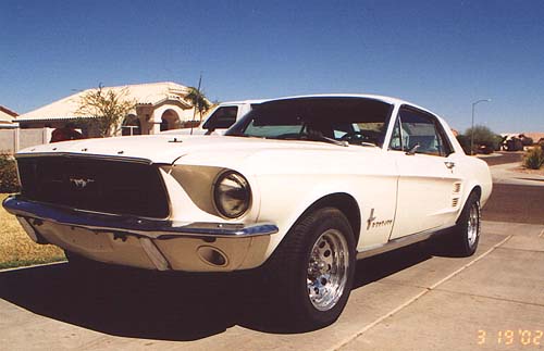 White first-gen Ford Mustang coupe, front three-quarter, with primer patches
