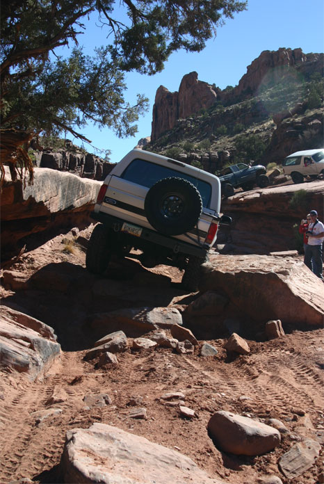 1993 Ford Bronco - Several vehicles traverse a challenging off-road path in a desert landscape under a clear blue sky.