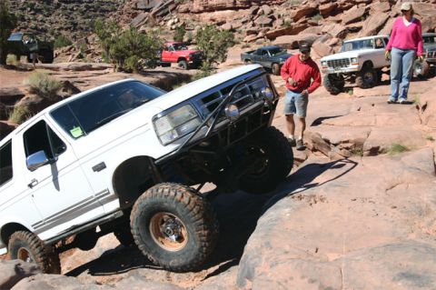 1993 Ford Bronco - A white 1993 Ford Bronco tackles a challenging off-road course with other vehicles in the background.