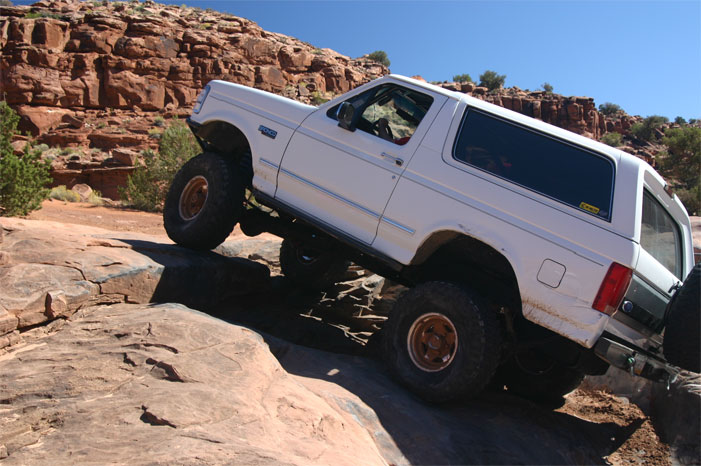 White 1993 Ford Bronco climbing over large rocks on an off-road trail