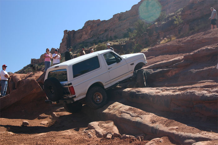 White 1992 Ford Bronco climbing rocky terrain, rear-mounted spare tire visible