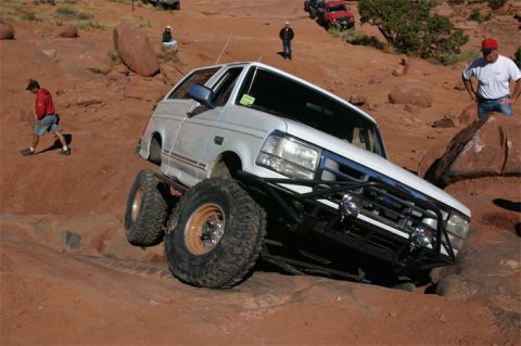 1993 Ford Bronco - A modified white Ford Bronco tackles a challenging off-road course in a desert landscape.