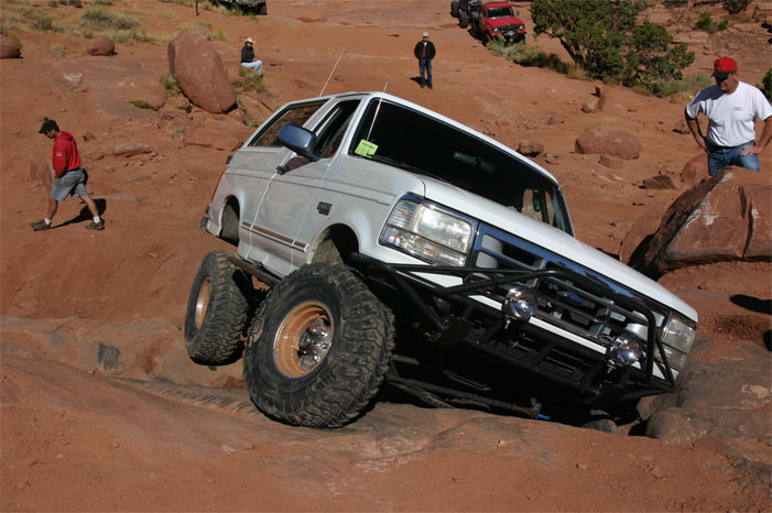 White Ford Bronco with off-road modifications navigating a rocky trail