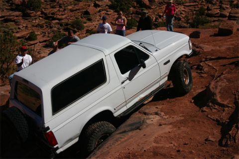 1993 Ford Bronco - A white 1993 Ford Bronco tackles a challenging off-road course with onlookers observing.