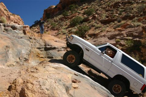1993 Ford Bronco - A white Ford Bronco navigates a challenging off-road course in a desert canyon landscape.