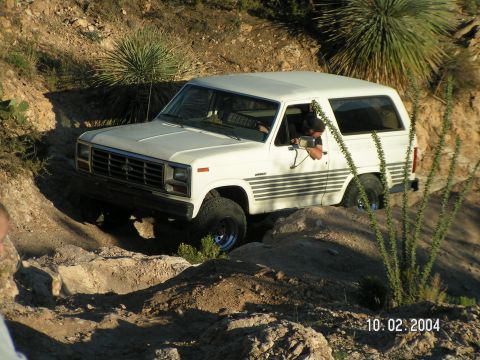 1983 Ford Bronco - White 1983 Ford Bronco tackling a challenging off-road trail with rocky obstacles.