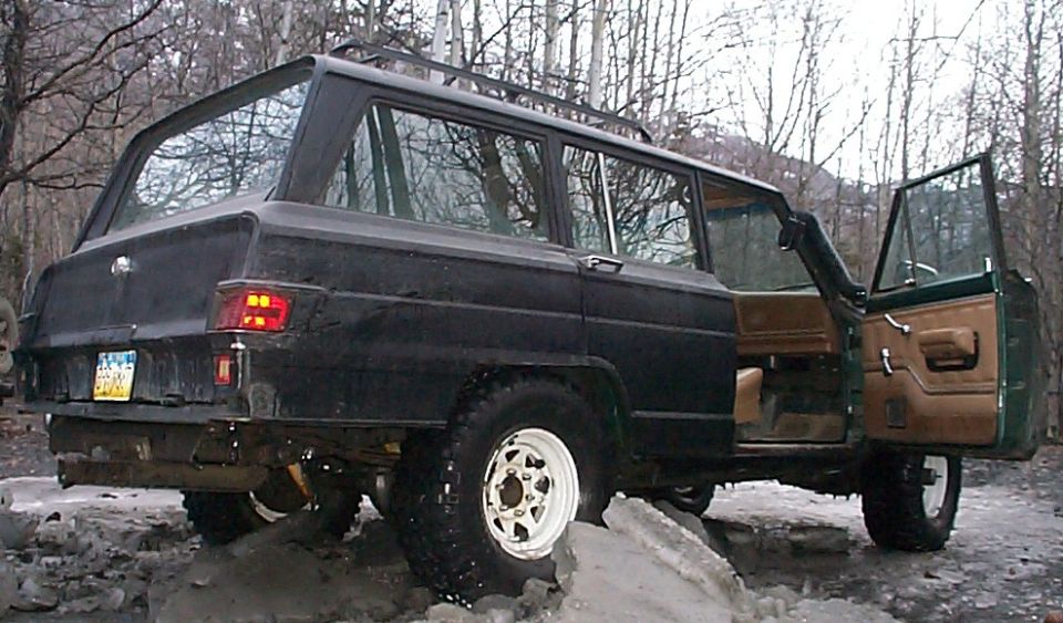 Rear three-quarter of a black lifted wagon with tan interior and white wheels on snowy ground