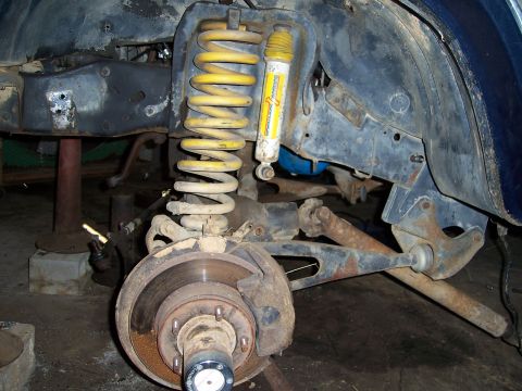 1983 Ford Bronco - Close-up of a vehicle's front suspension system, a yellow coilover shock and disc brake assembly.