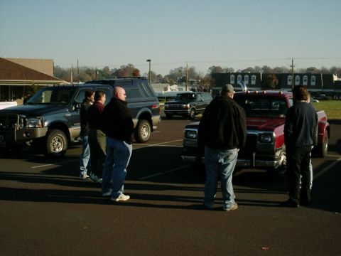 2002 Ford F-250 - A group of people gathered around several trucks and SUVs in a parking lot on a sunny day.