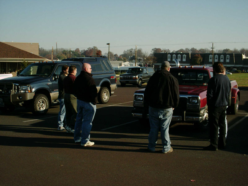 Men standing in parking lot between a lifted gray Ford Super Duty and a red Dodge dually