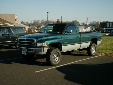 2002 Ford F-250 - A green and silver pickup truck is parked in a lot next to a dark SUV.