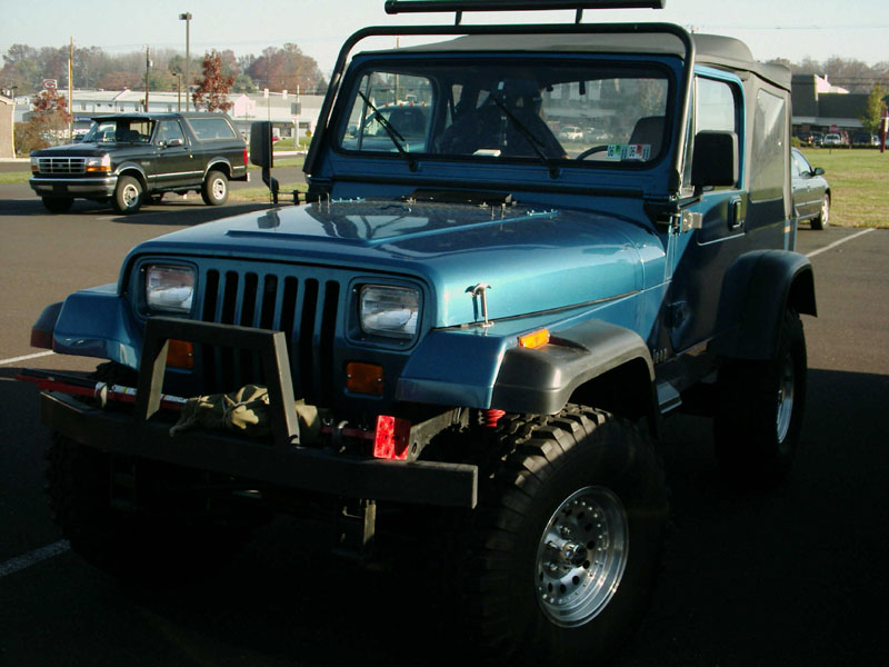 Lifted blue Jeep Wrangler YJ with soft top and mud tires, front three-quarter view
