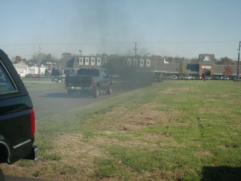 2002 Ford F-250 - A black 2002 Ford F-250 pickup truck is seen from the side, emitting a large cloud of black exhaust smoke.