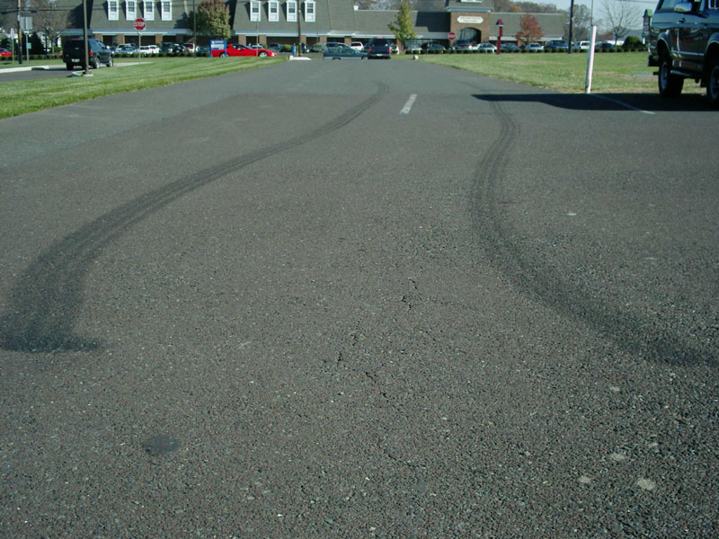 Long dual tire burnout marks curving on asphalt road with lifted truck at right edge