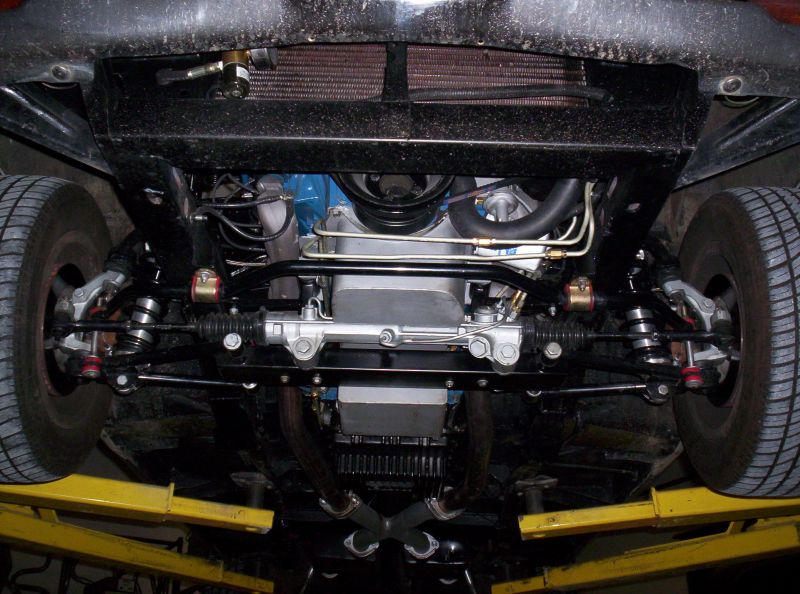 Underside of car front end showing steering rack, suspension, sway bar and dual exhaust on a yellow lift