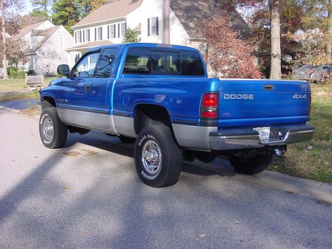 1989 Ford Bronco - A blue Dodge Ram pickup truck is parked on the side of a street in front of houses.