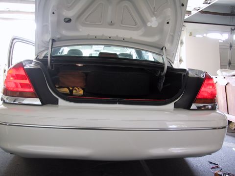 2003 Ford Crown Victoria - Rear view of a white 2003 Ford Crown Victoria with its trunk open, revealing a spare tire and some bags.