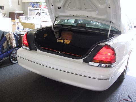 2003 Ford Crown Victoria - The rear of a white 2003 Ford Crown Victoria with its trunk open, showing stored items.