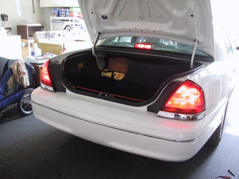 2003 Ford Crown Victoria - The rear of a white 2003 Ford Crown Victoria sedan is shown with its trunk open, revealing the interior storage space.