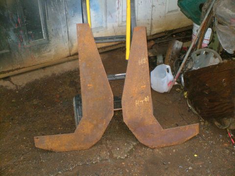 1989 Ford Bronco - A pair of thick, flame-cut rusty steel plates standing on a dirt shop floor, shaped as mirror-image end pieces for a fabricated bumper or b…