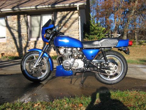 1985 Ford Crown Victoria LTD - A blue Suzuki motorcycle is parked on a wet driveway in front of a stone-sided house.