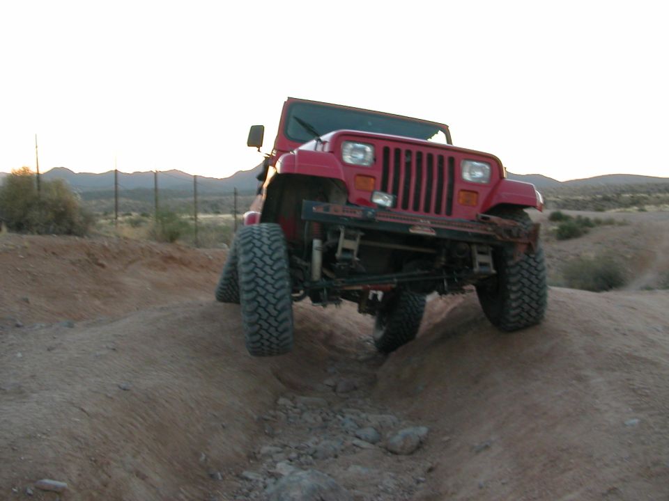 Red Jeep Wrangler YJ flexing over a rocky desert ditch, front view