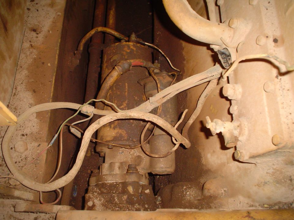 Starter motor with heavy wiring and hoses attached, covered in dirt
