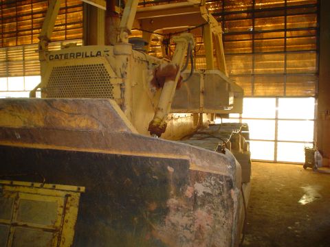 1966 International School Bus - A large yellow Caterpillar bulldozer sits inside a garage with a bright, open door in the background.